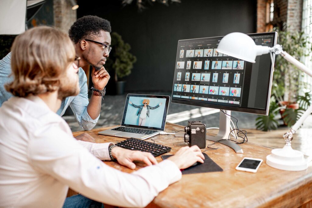 Two male photographers choosing woman's portraits at the working place with two computers in the studio